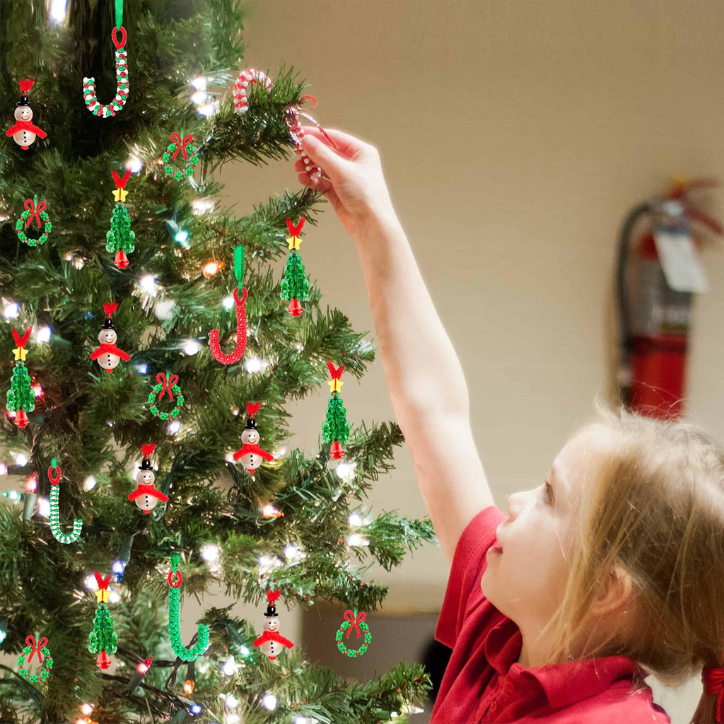 Child decorating a Christmas tree with handmade beaded ornaments including snowmen, candy canes, wreaths, and trees.