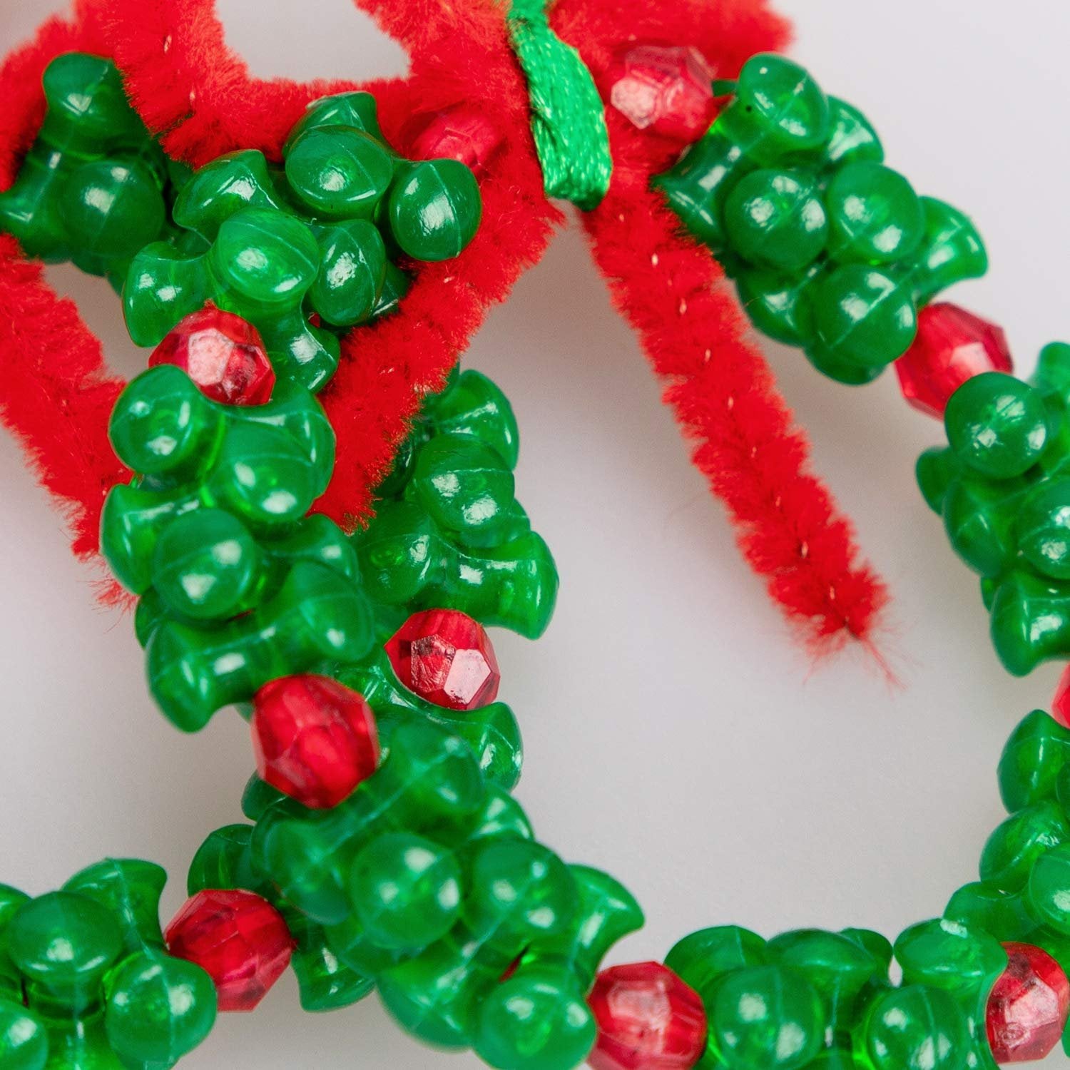 Close-up of a handmade Christmas ornament kit with green beads and red pipe cleaners forming a wreath shape.