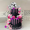 Two-tier black cake decorated with pink drip icing and a disco ball cake topper set featuring mirror balls, foam spheres, and star picks.
