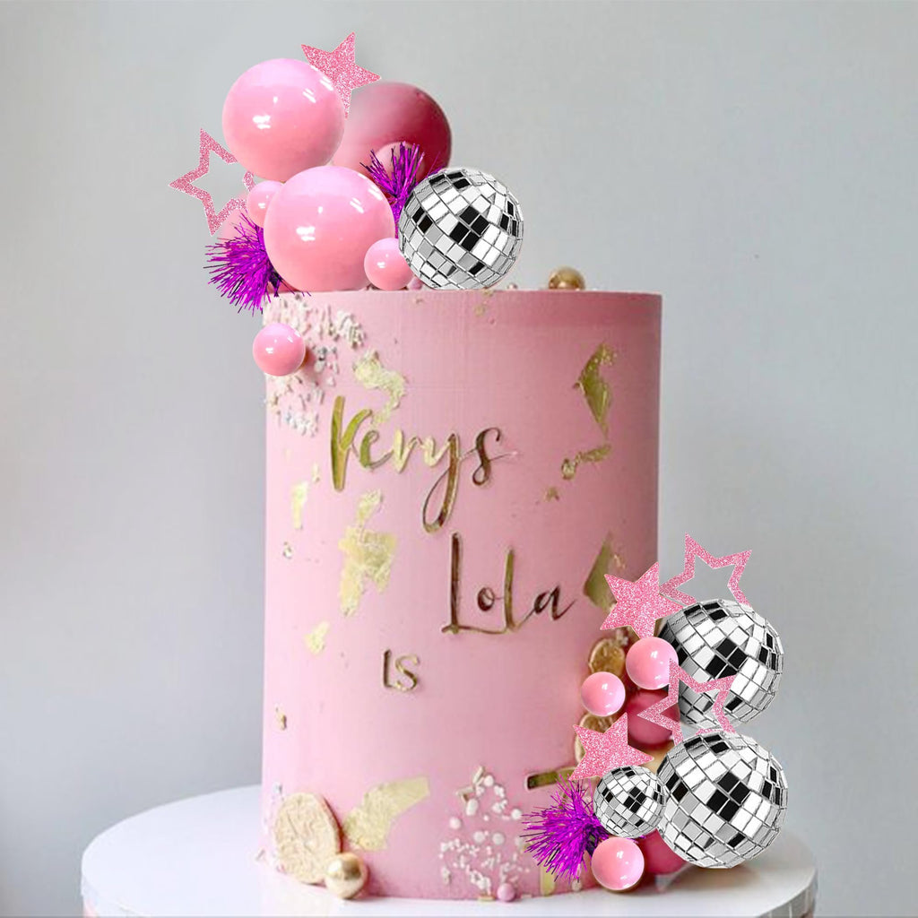 Pink cake decorated with disco ball toppers, pink spheres, glitter stars, and gold leaf accents. Text reads 'Kerys Lola LS'.