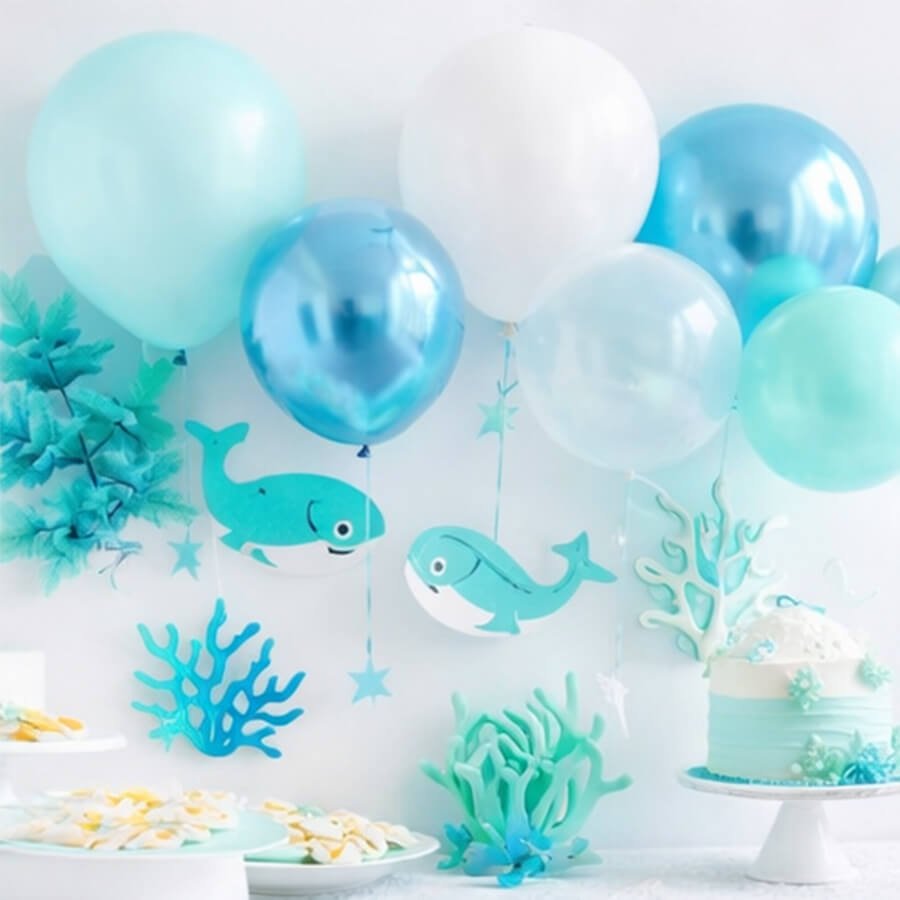 Under the sea themed party decorations with balloons, whale cutouts, coral, and cake.