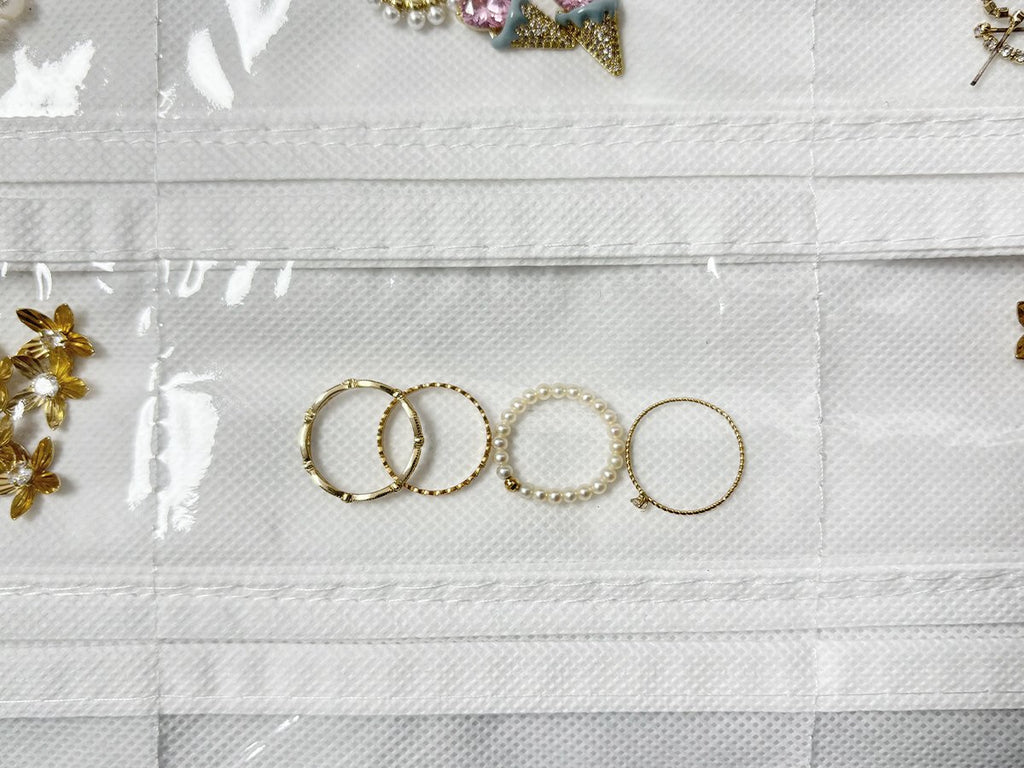 Close-up of a white hanging jewelry organizer with transparent pockets showing gold rings and pearl bracelets.