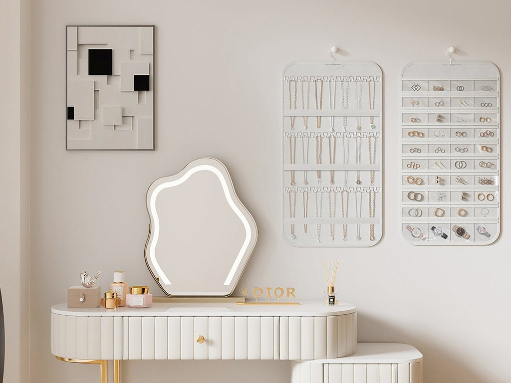 Two white hanging jewelry organizers filled with necklaces, rings, earrings, and watches on a wall above a vanity.