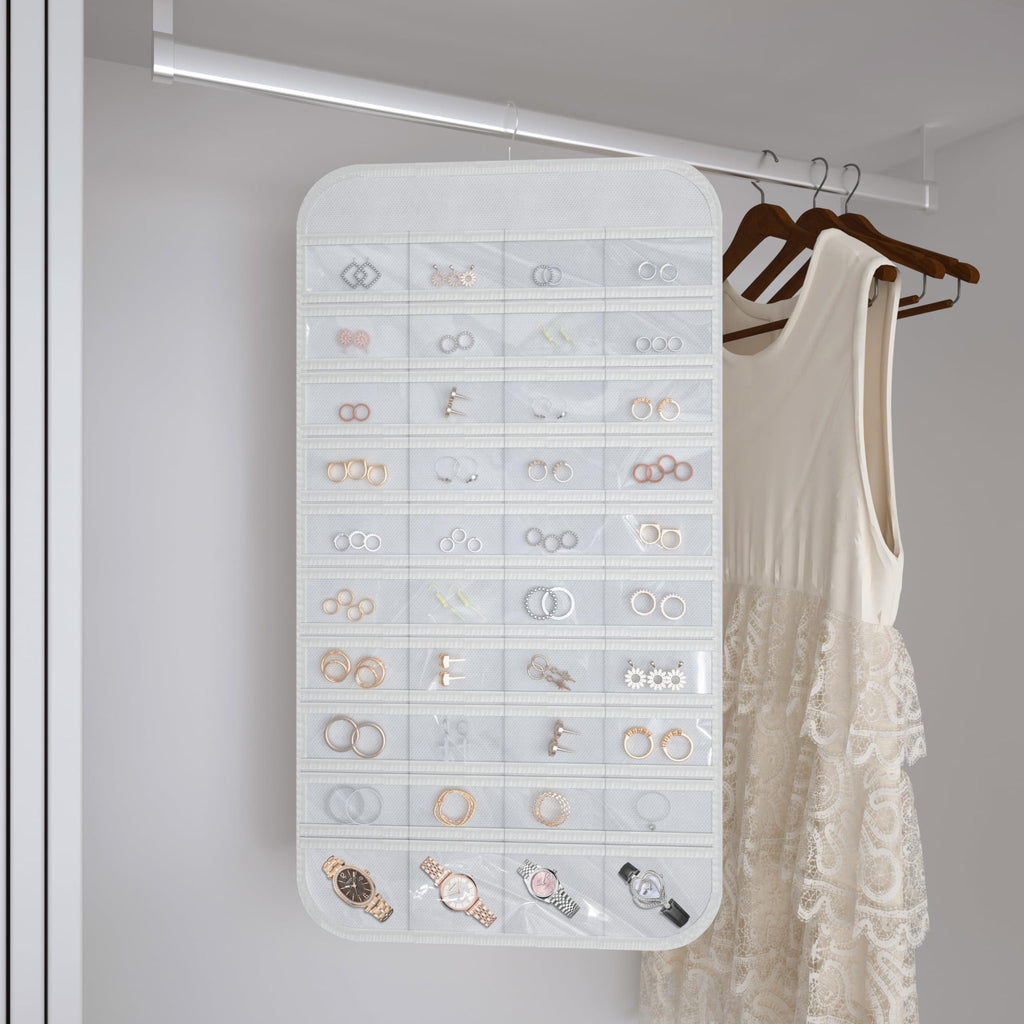 White hanging jewelry organizer with 40 clear pockets filled with jewelry and watches, shown in a closet next to a dress.