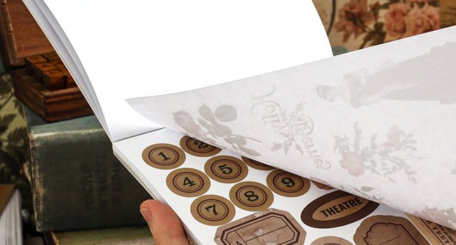 Close-up of a vintage nature forest ephemera book with pre-cut washi stickers and scrapbook papers being flipped.