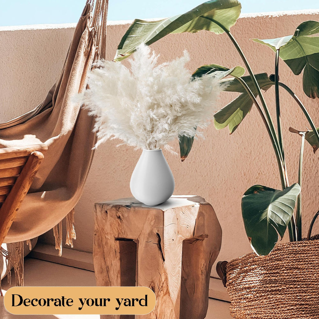 White pampas grass in a white vase on a wooden stool, with a hammock and plants in the background.