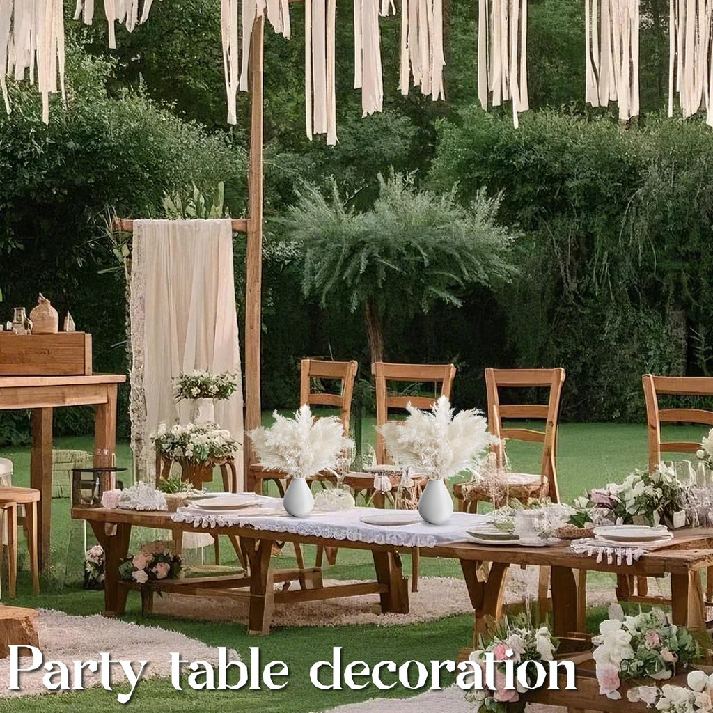 Outdoor wedding reception table setting with white pampas grass arrangements in vases.