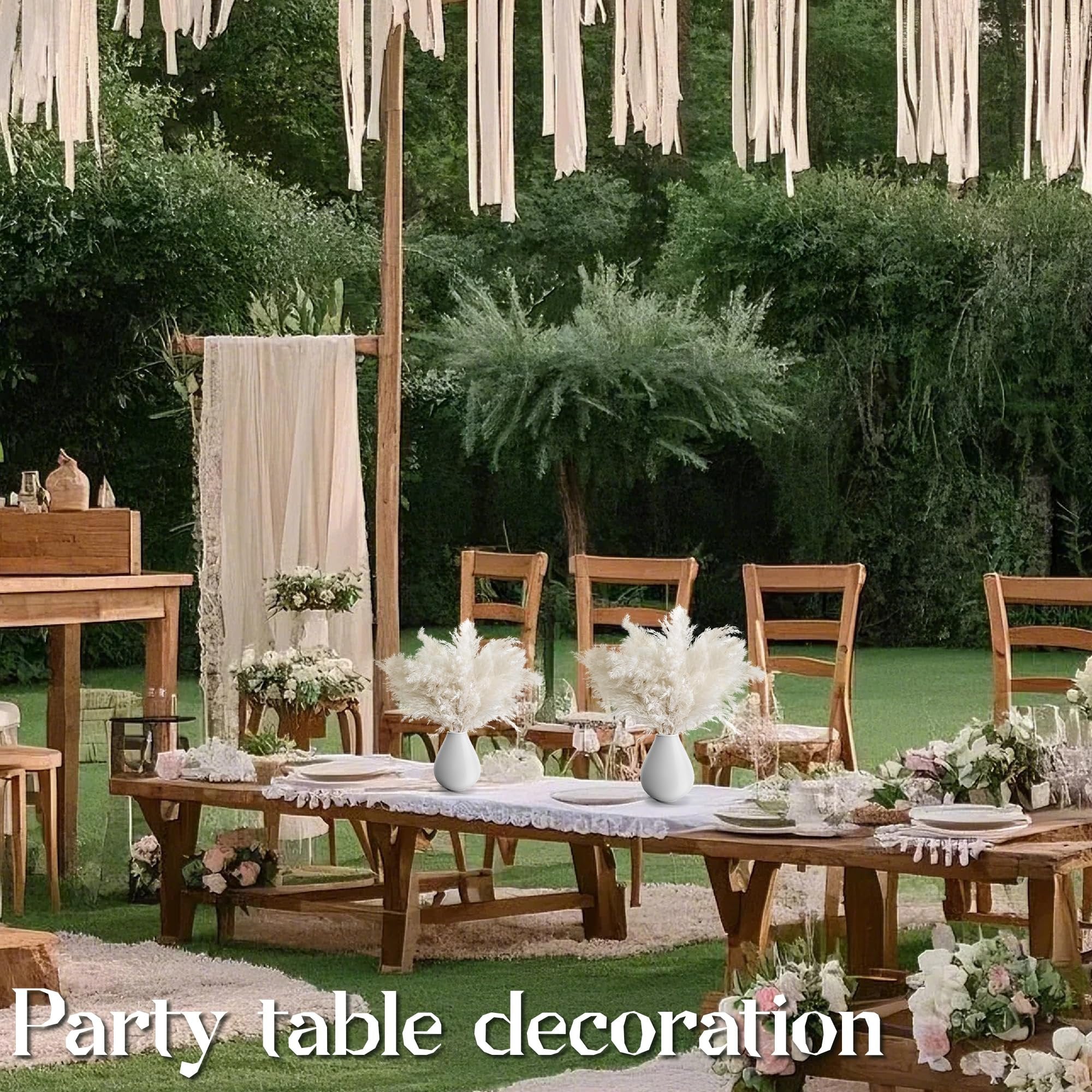 Outdoor wedding reception table setting with white pampas grass arrangements in vases.