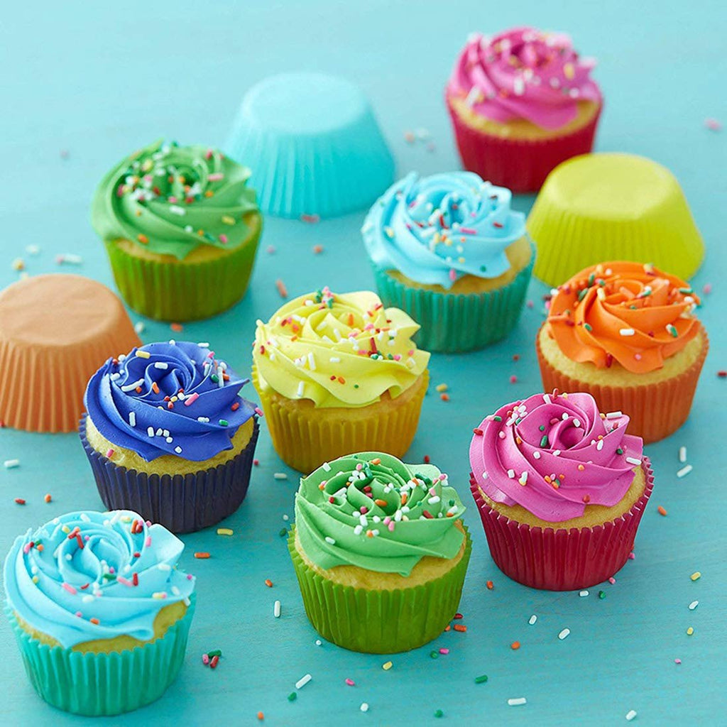 Assortment of colorful frosted cupcakes with sprinkles and paper liners scattered on a blue surface.