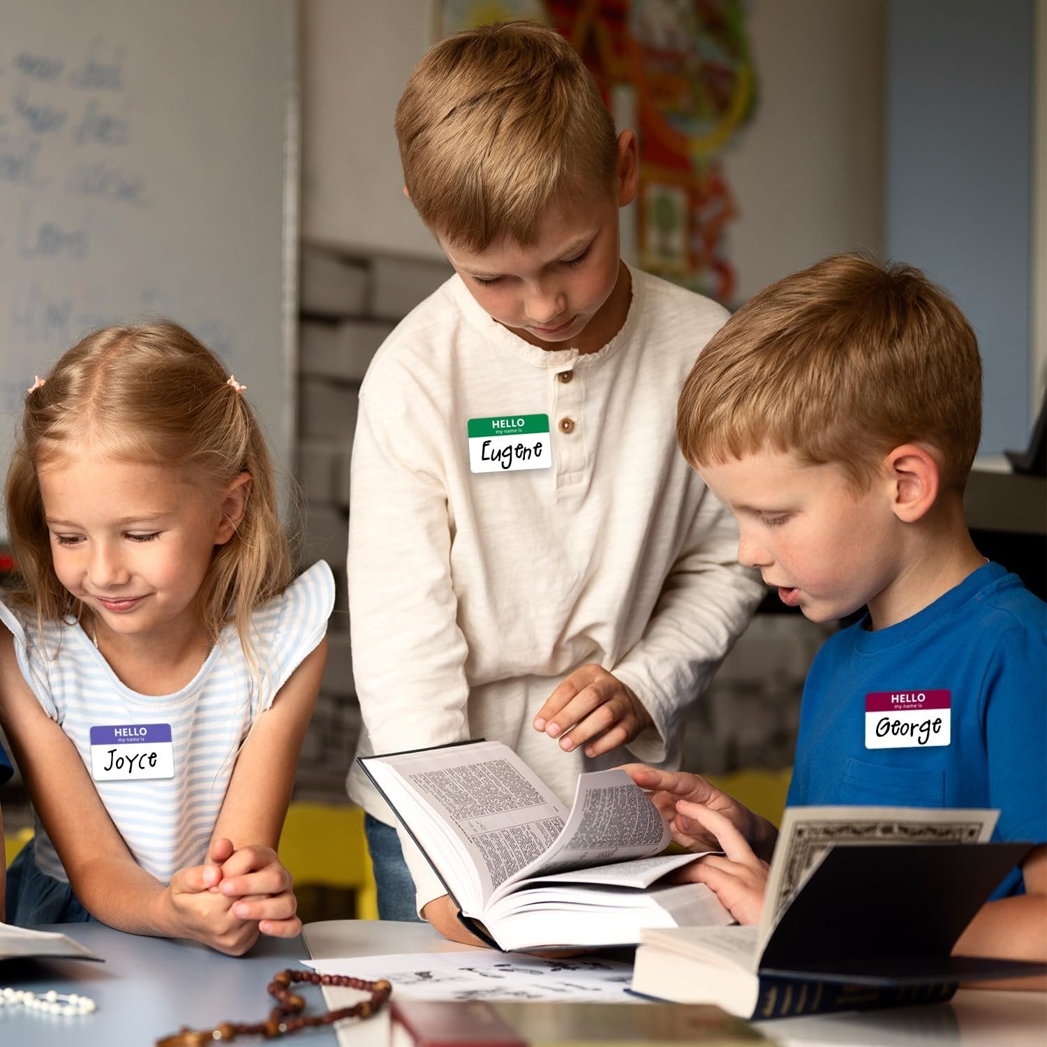 Three children gathered around books, wearing name tags with their names written on them.