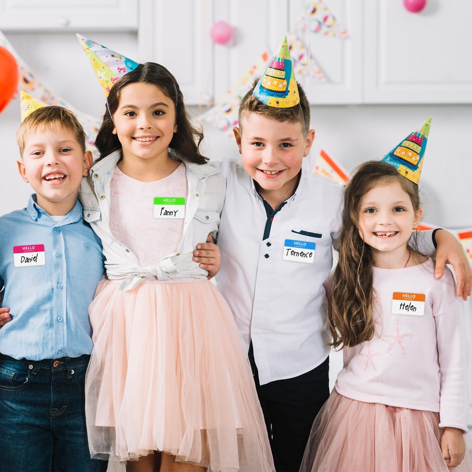 Four smiling children wearing party hats and name tags at a birthday party.