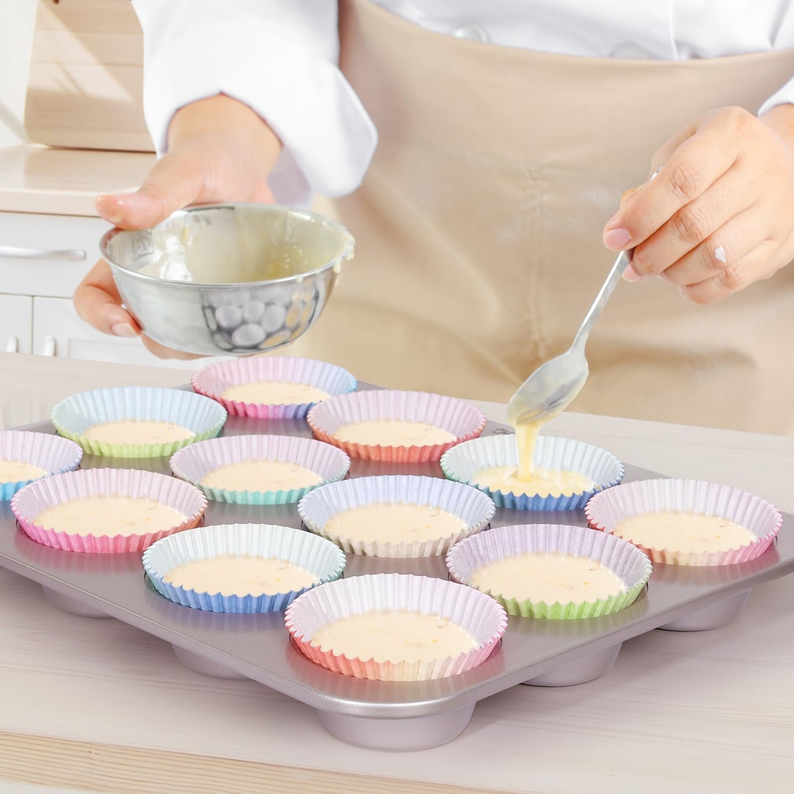Person pouring cupcake batter into colorful paper liners in a muffin tin
