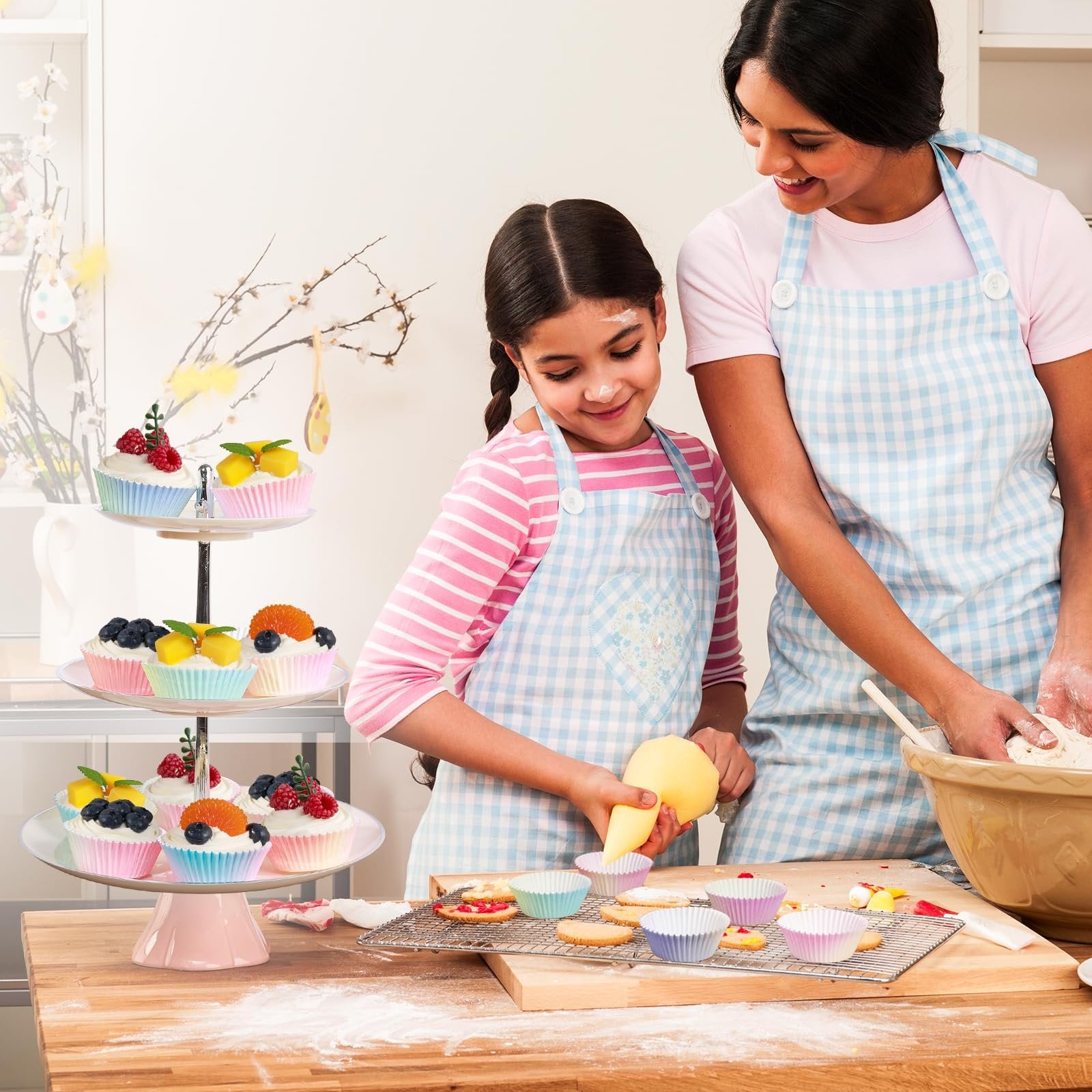 Mother and daughter baking cupcakes together, with a tiered stand displaying decorated cupcakes.