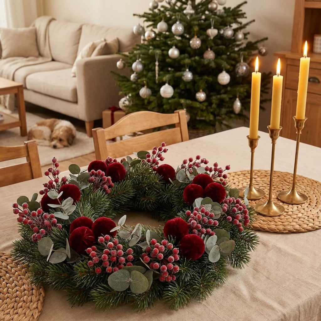 Christmas wreath with red berries and pine branches on a table with candles and a Christmas tree in the background