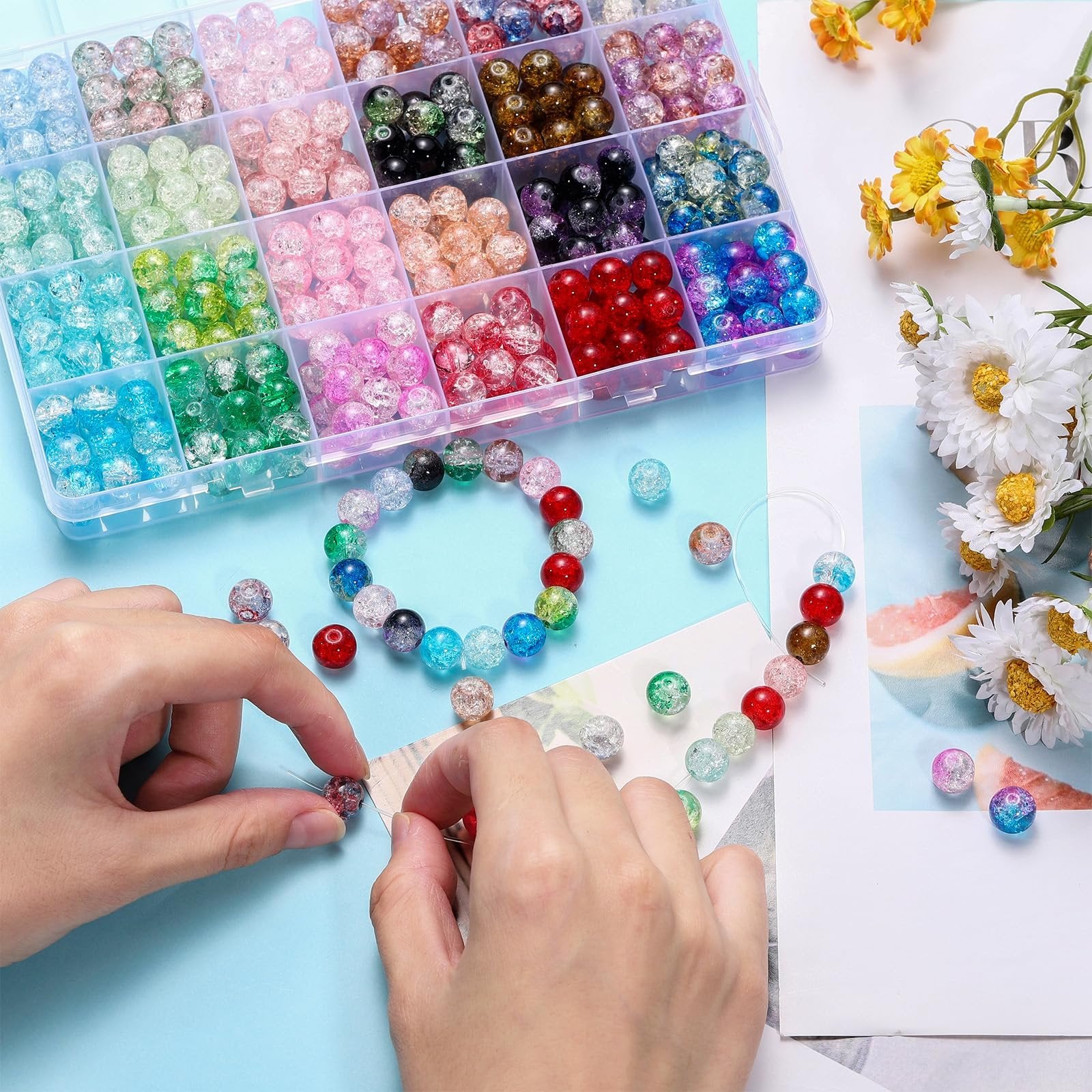 Hands stringing colorful crackle glass beads from a divided storage box, with a bracelet and loose beads scattered around.
