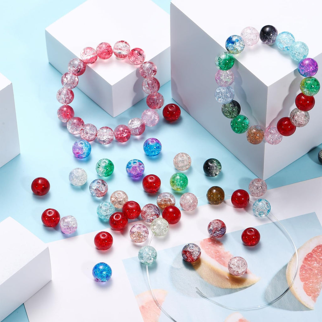 Assorted crackle glass beads in various colors scattered around two bracelets on white blocks