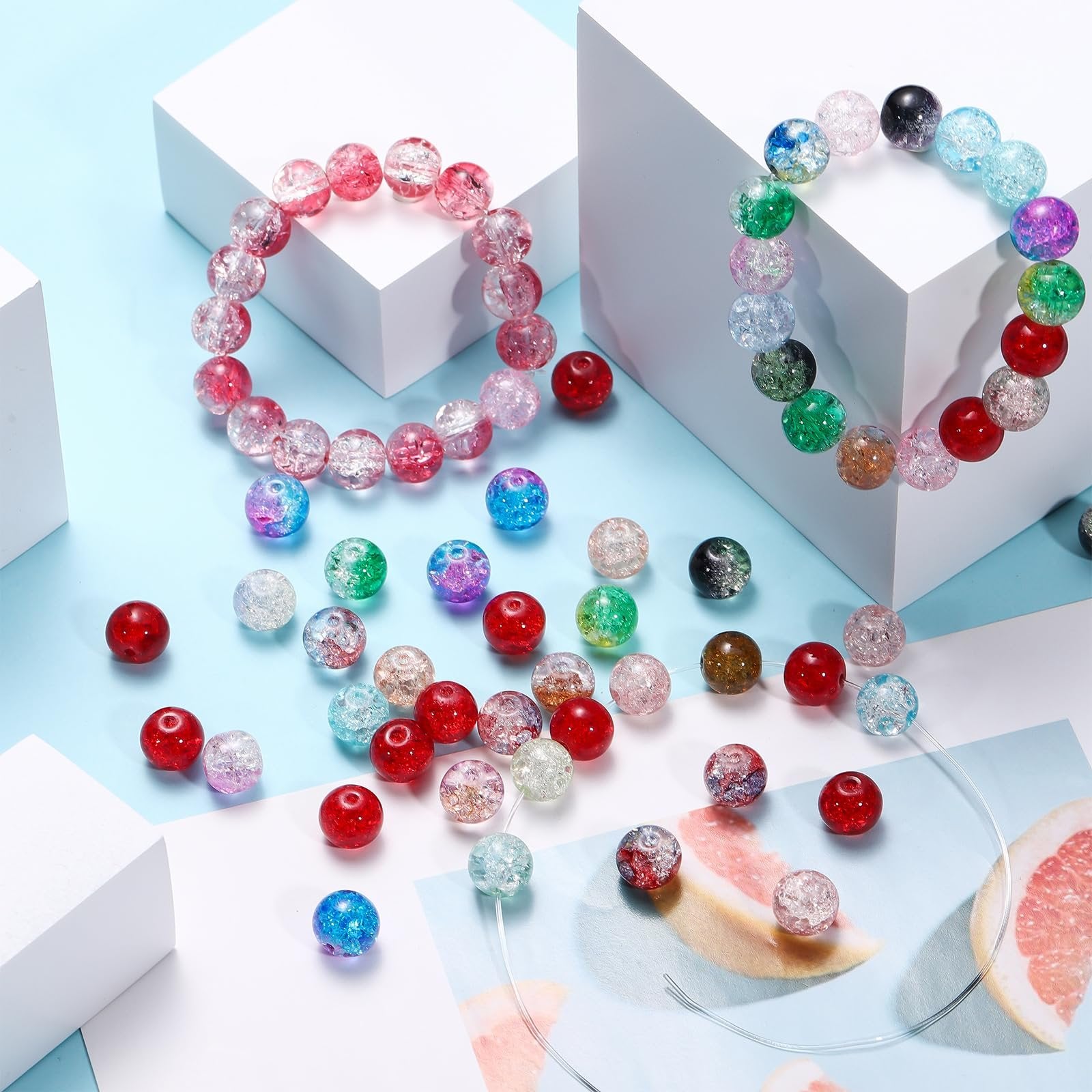 Assorted crackle glass beads in various colors scattered around two bracelets on white blocks