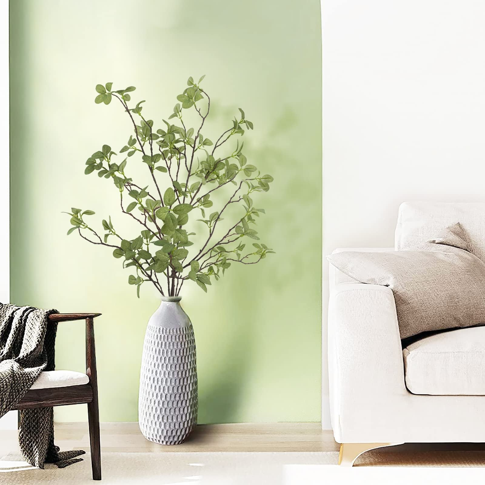 Artificial ficus twig leaf greenery stems in a decorative vase on a wooden surface next to a chair and sofa.