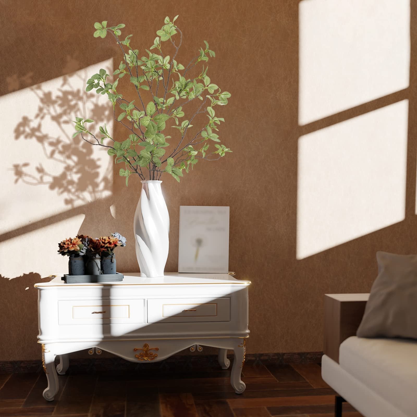 Artificial ficus twig greenery stems in a white vase on a white table, with shadows cast on the wall.