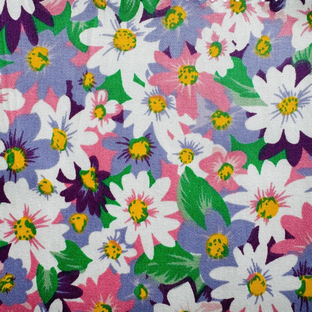 Close-up of a floral pattern fabric with white, pink, and purple daisies on a white background.