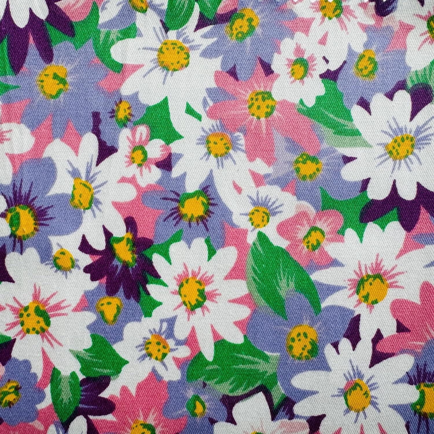 Close-up of a floral pattern fabric with white, pink, and purple daisies on a white background.