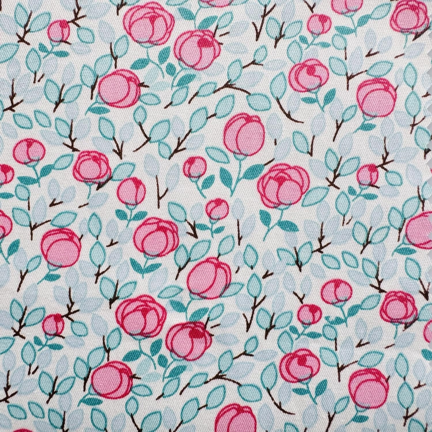 White fabric with a repeating pattern of pink roses and light blue leaves on thin brown branches.