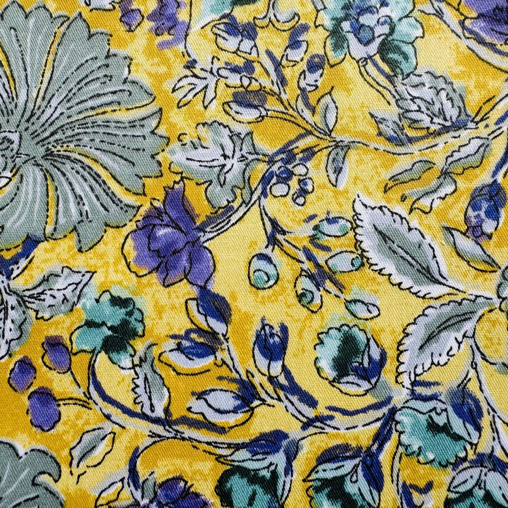 Close-up of yellow cotton fabric with a floral pattern in blue, green, and gray.