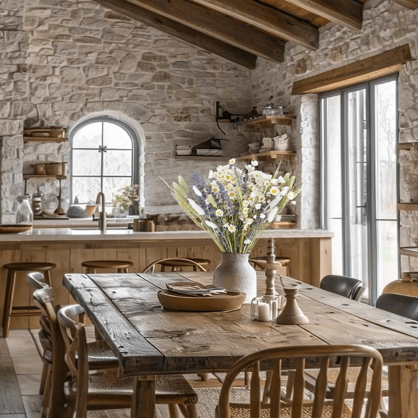 Dried flower bouquet with lavender, daisies, and wheat in a vase on a rustic wooden table in a kitchen.