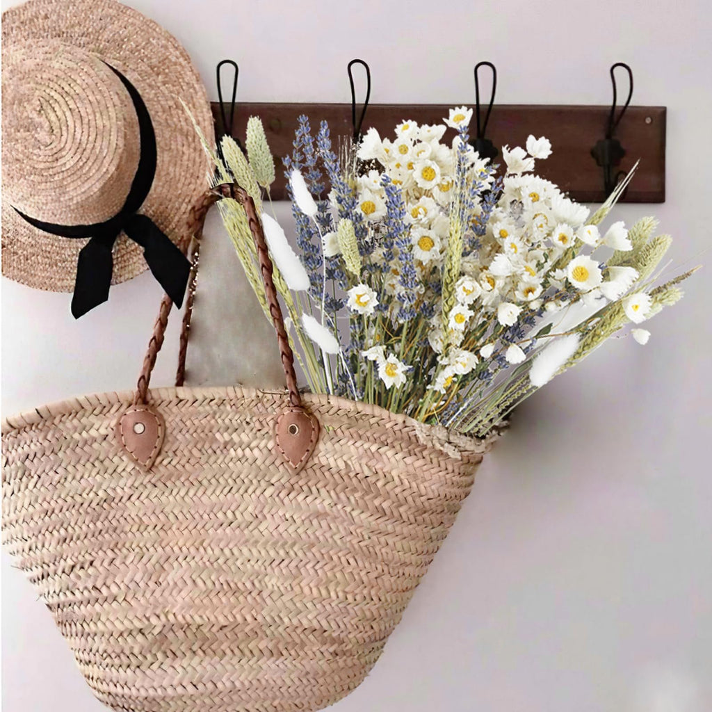 Straw hat with black ribbon and woven tote bag filled with dried flowers hanging on a wall hook