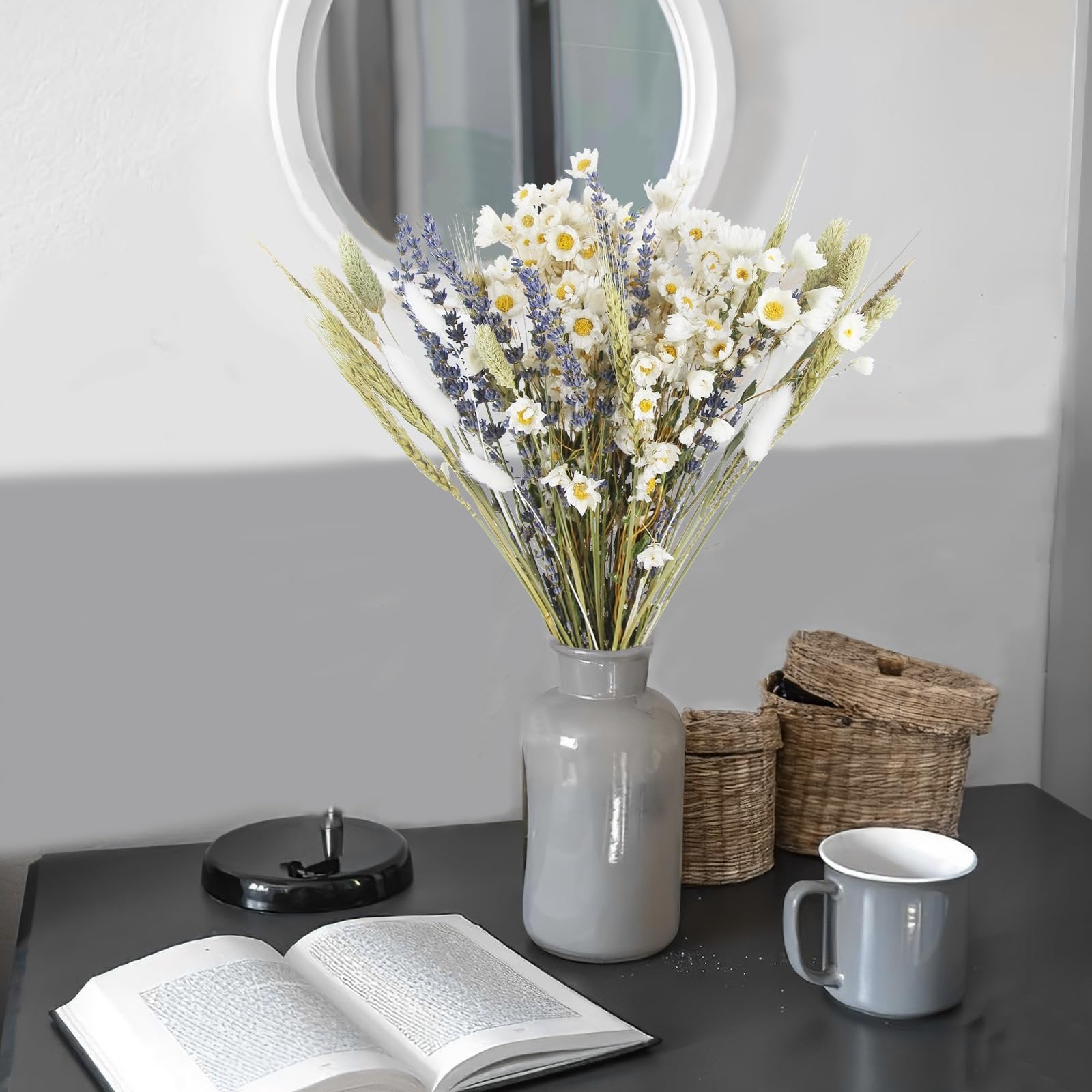 Dried flower bouquet with lavender and daisies in a grey vase on a desk with an open book and woven baskets.