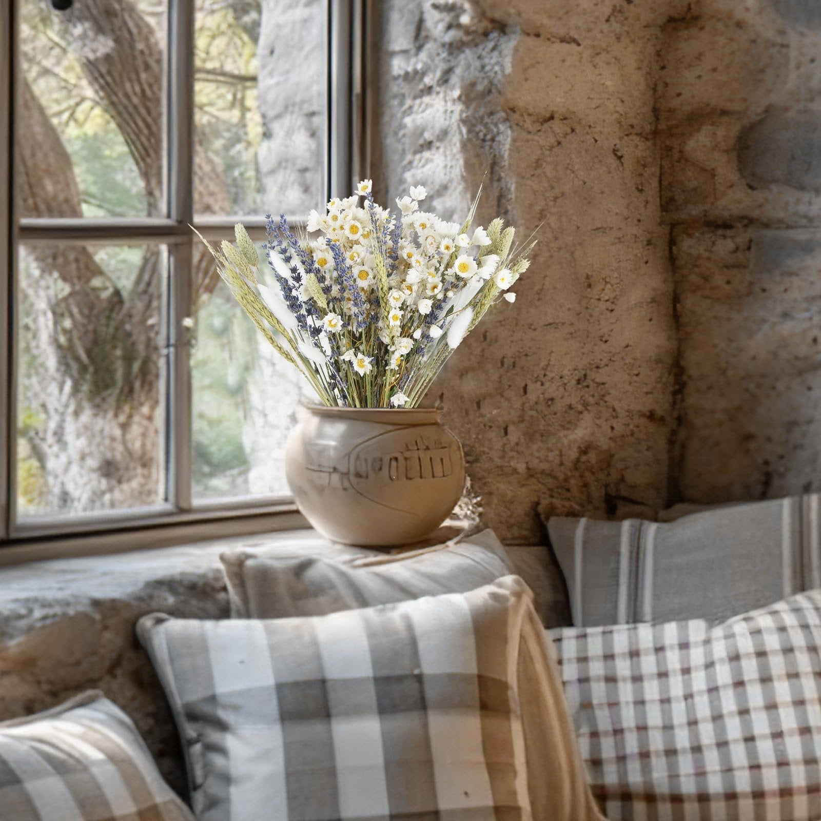 Dried flower bouquet with lavender and daisies in a ceramic vase on a windowsill with pillows