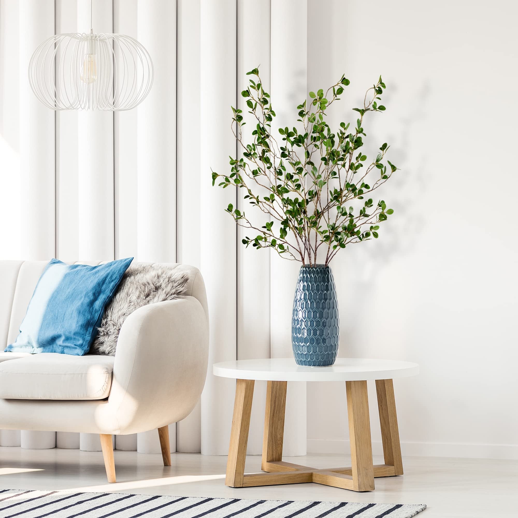 Artificial ficus branches in a blue vase on a white coffee table next to a sofa