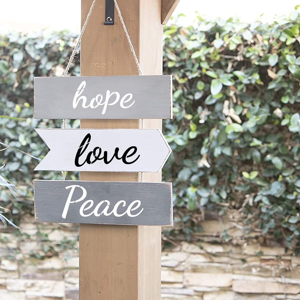 Three wooden signs with inspirational words 'hope', 'love', and 'Peace' hanging on a post outdoors.