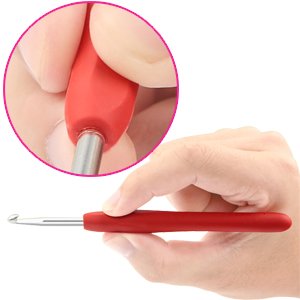 Close-up of a red ergonomic crochet hook with a metal tip, held by a hand. Inset shows a finger pressing the rubber handle.