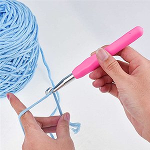 Crocheting with a pink ergonomic hook and blue yarn, showing how to loop yarn onto the hook.