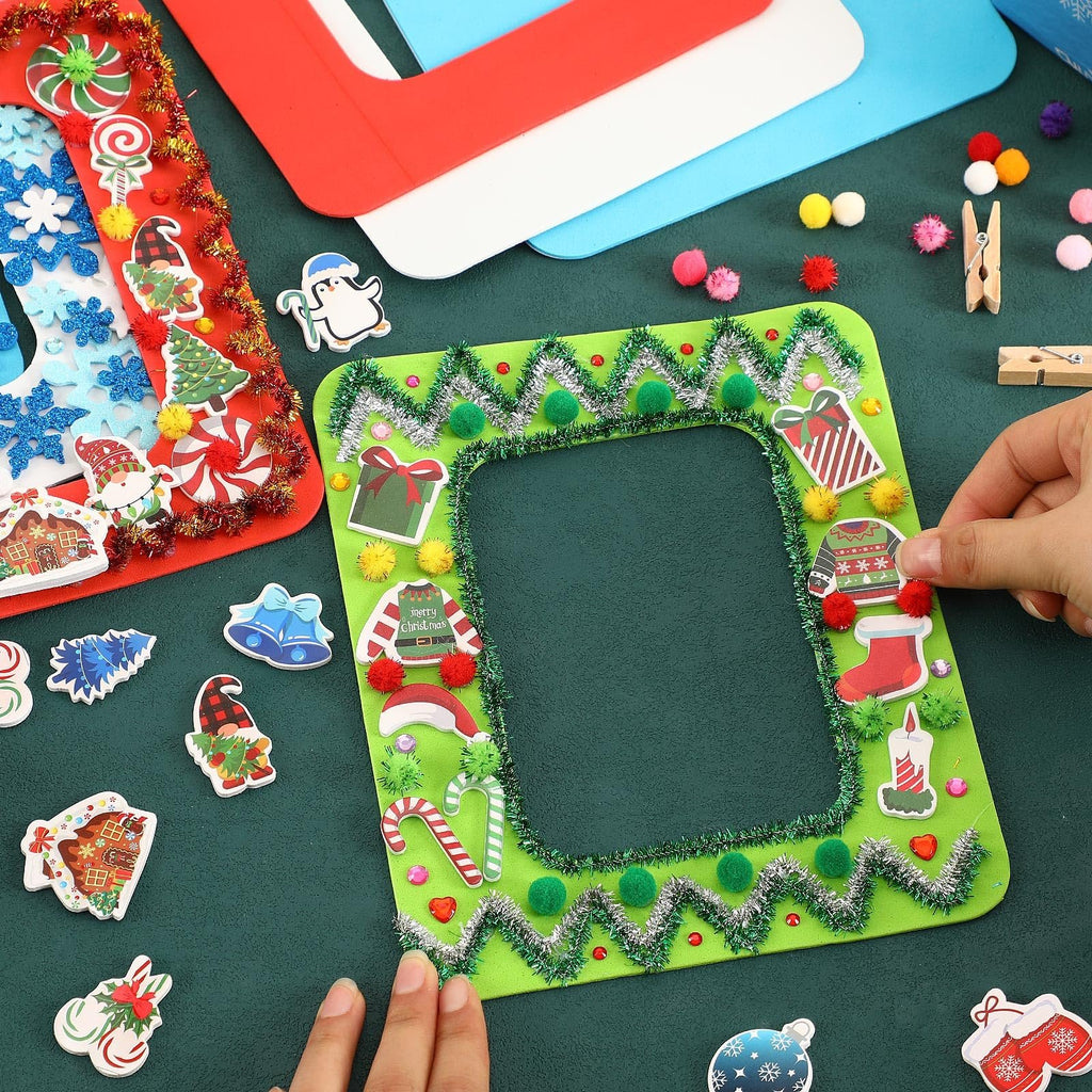 Hands decorating a green foam Christmas picture frame with festive stickers and tinsel, surrounded by craft supplies.