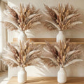 Four vases filled with dried pampas grass and bunny tail decor arranged on a wooden shelf and table.