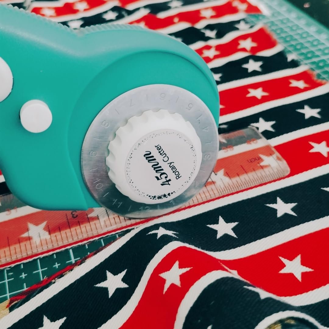 Close-up of a turquoise 45mm rotary cutter on striped fabric with stars, next to a ruler and cutting mat.