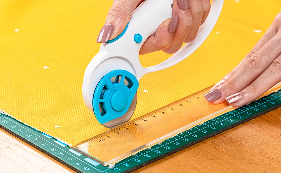 Hands using a rotary cutter and ruler to cut yellow fabric on a cutting mat