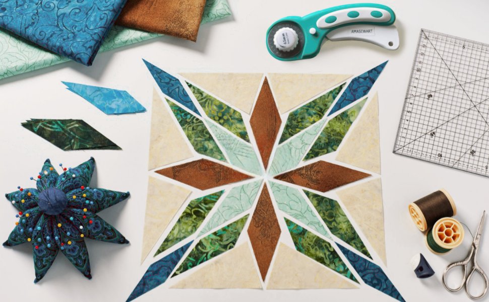 Rotary cutter, fabric scraps, pincushion, quilt block, and sewing notions arranged on a white surface.