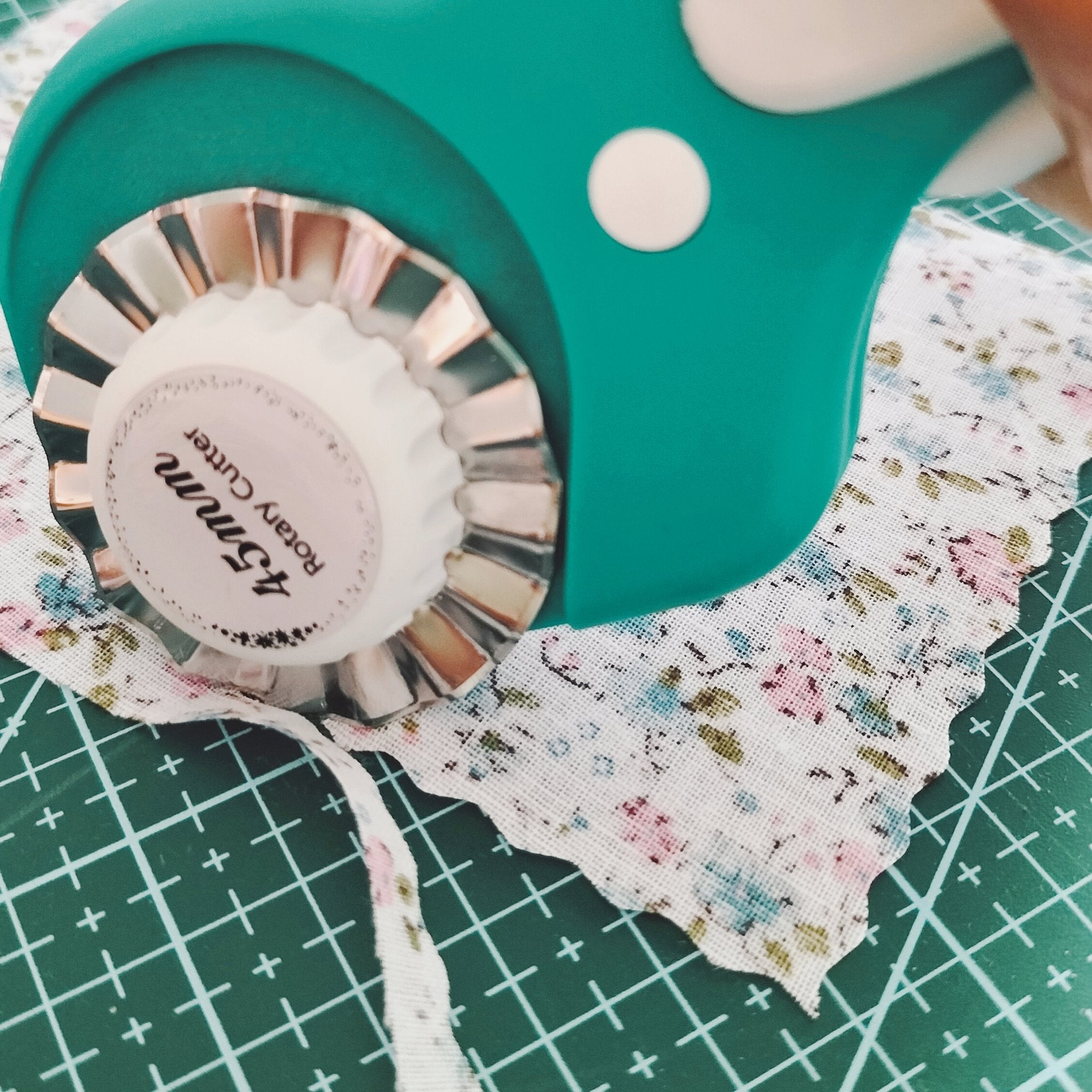 Close-up of a teal rotary cutter with a 45mm blade cutting floral fabric on a green cutting mat.