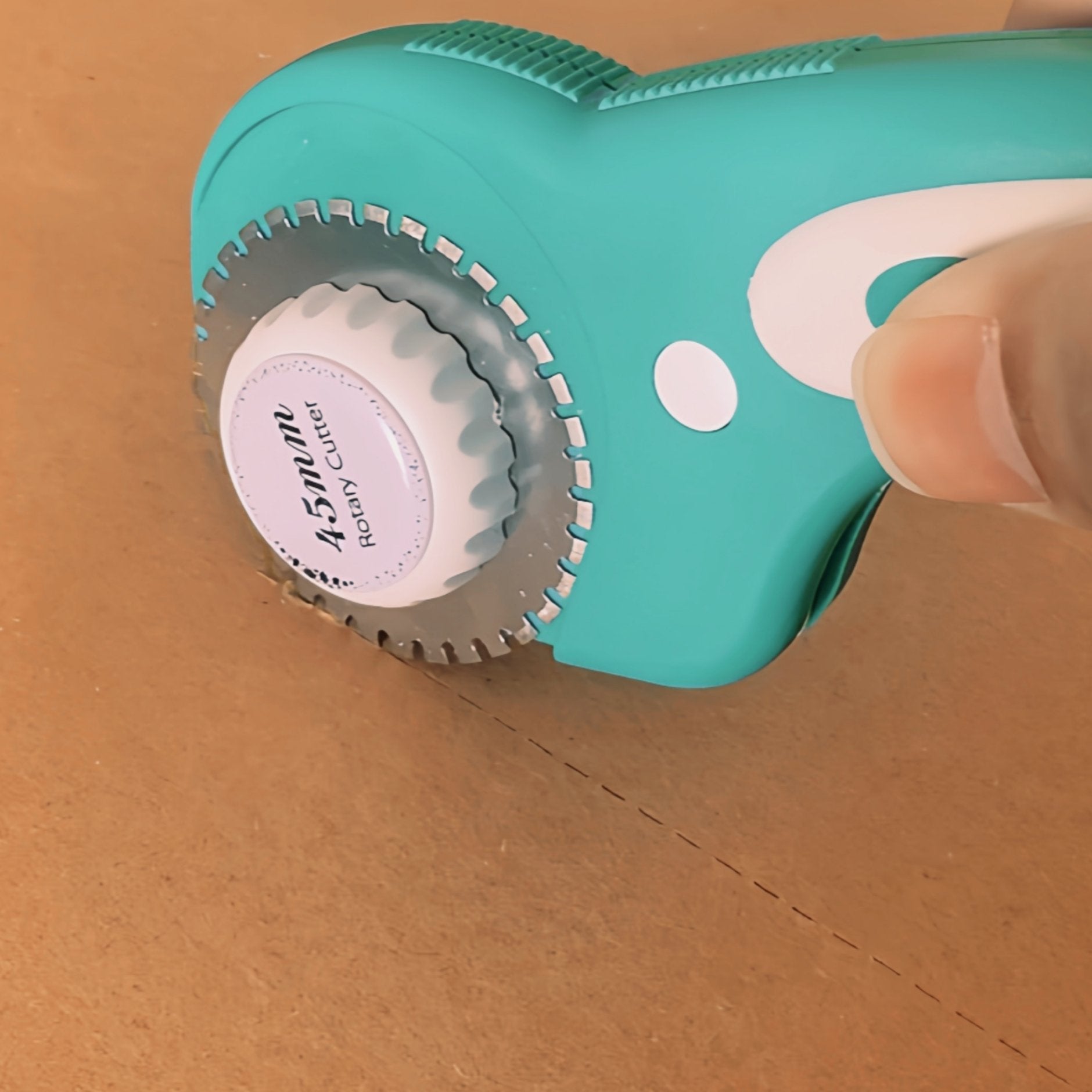 Close-up of a teal rotary cutter with a white dial cutting a dashed line on a brown surface.