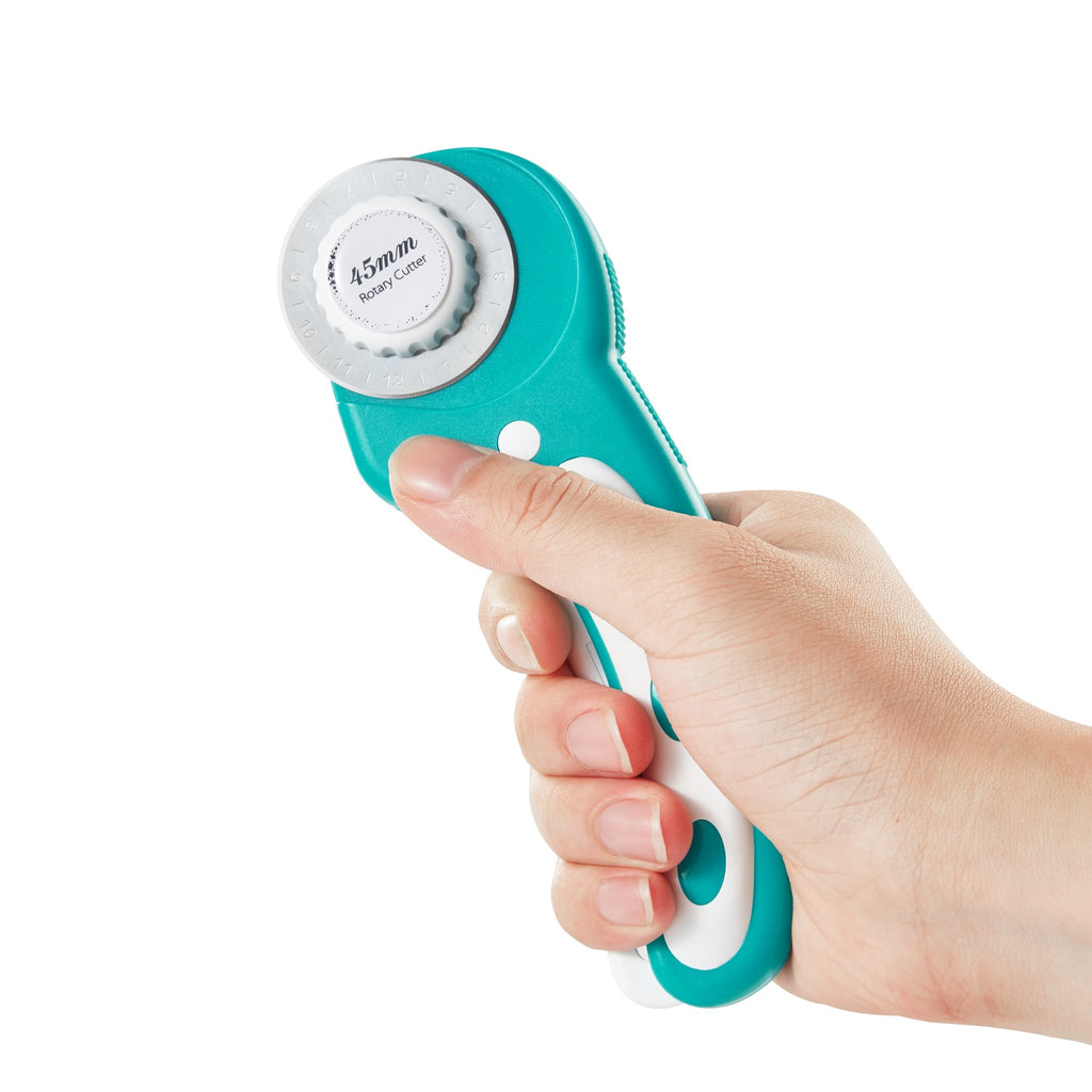 Hand holding a teal and white 45mm rotary cutter with a white background. The blade guard has measurement markings.