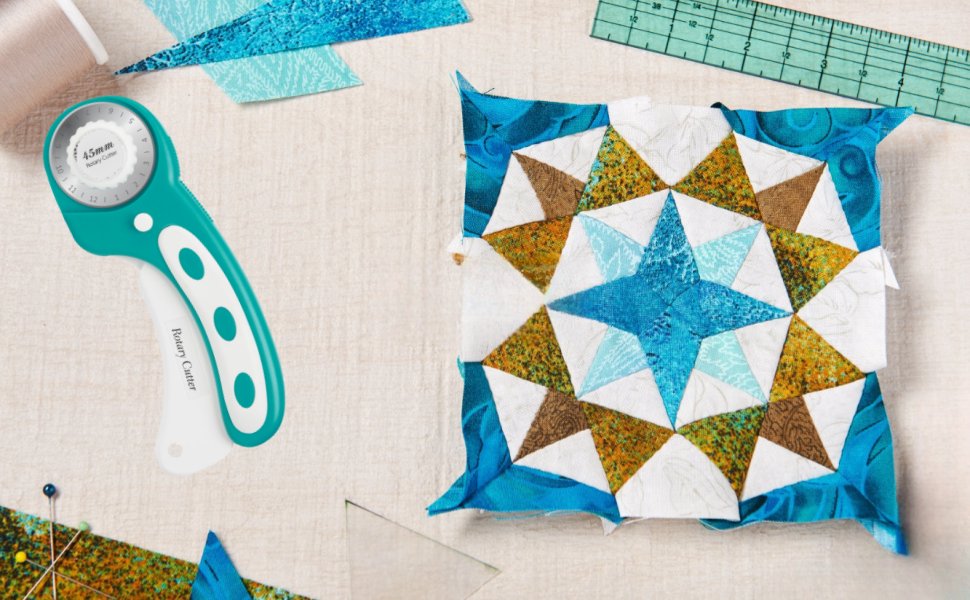 Teal rotary cutter and a star-patterned fabric quilt block on a light textured surface with sewing notions.