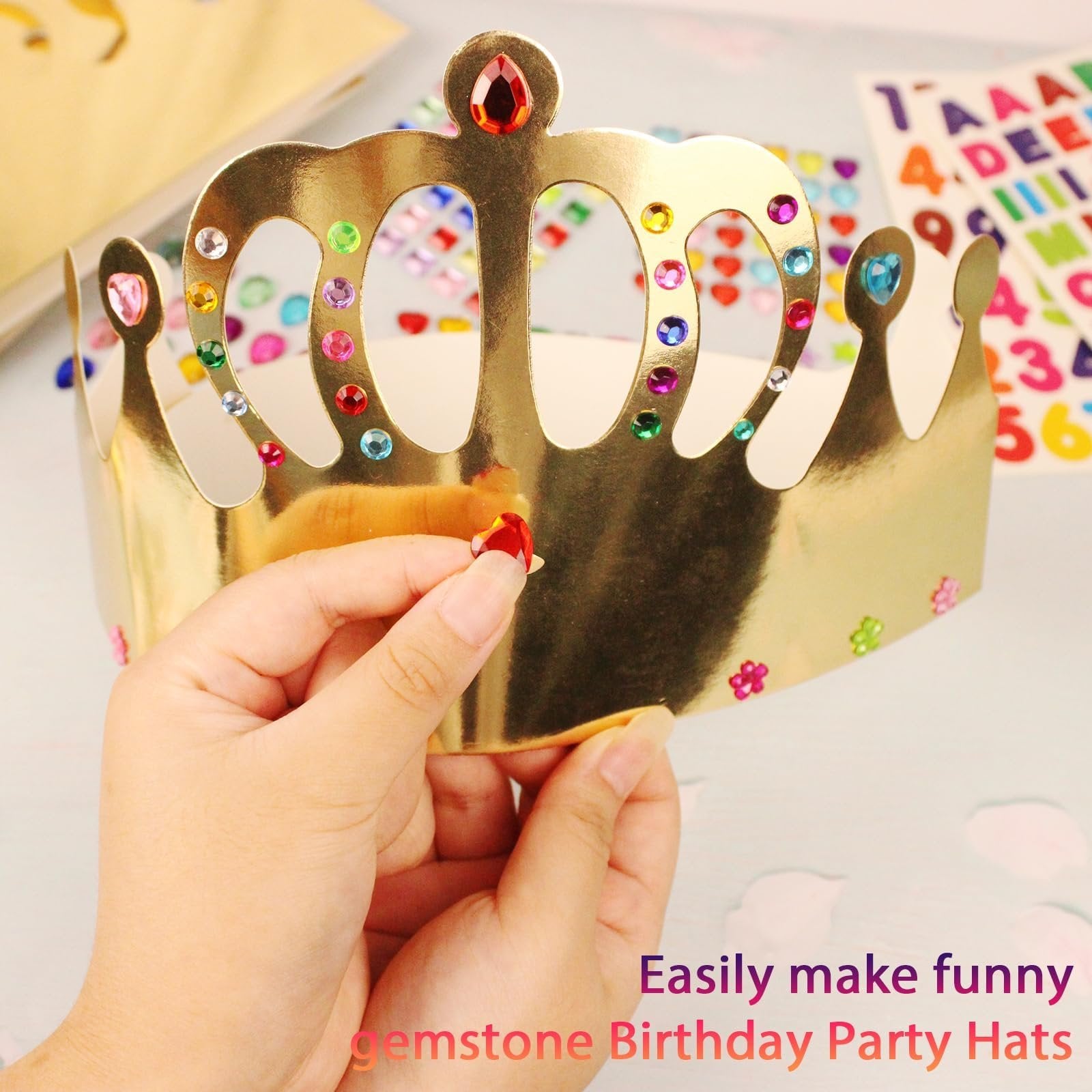 Hand decorating a gold paper crown with colorful adhesive gems and stickers for party hats.