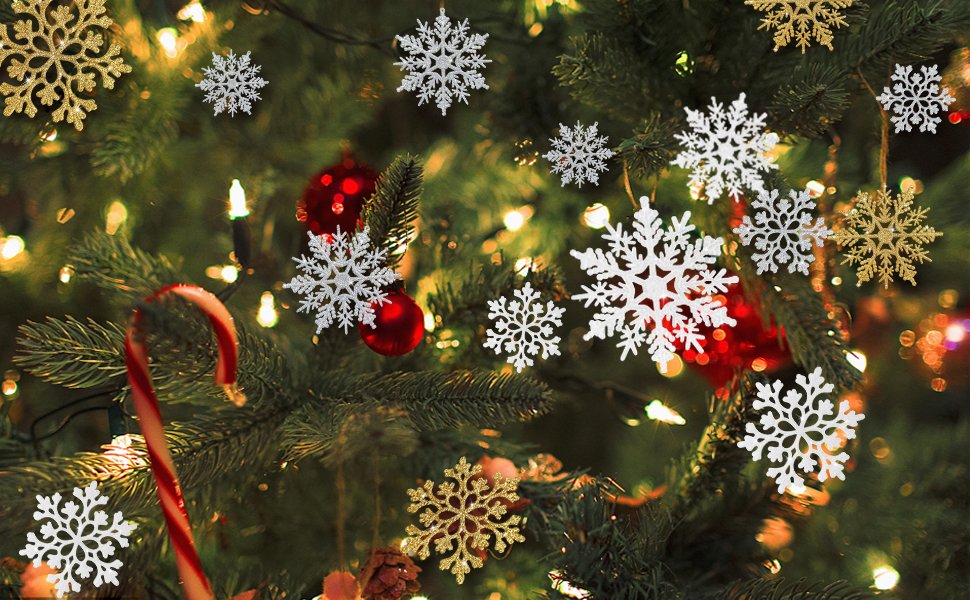 Assorted white and gold glitter snowflake ornaments hanging on a Christmas tree with lights and red baubles.