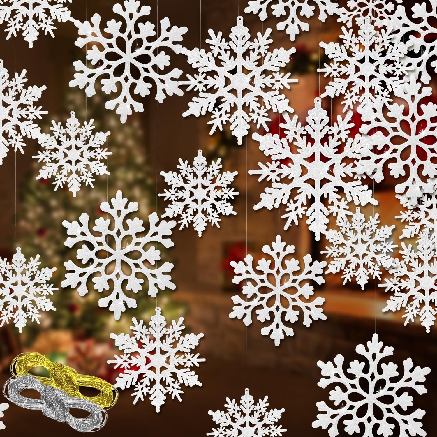 White glitter snowflake ornaments of various sizes hanging with spools of silver and gold rope on a blurred background.