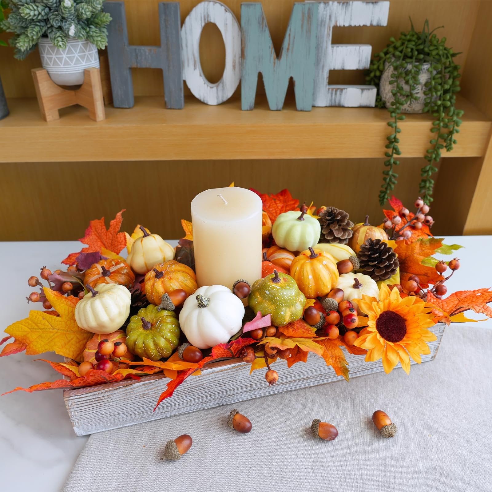 Fall harvest decor centerpiece with assorted mini pumpkins, gourds, pinecones, acorns, berries, and maple leaves arranged in a wooden box with a cream candle.