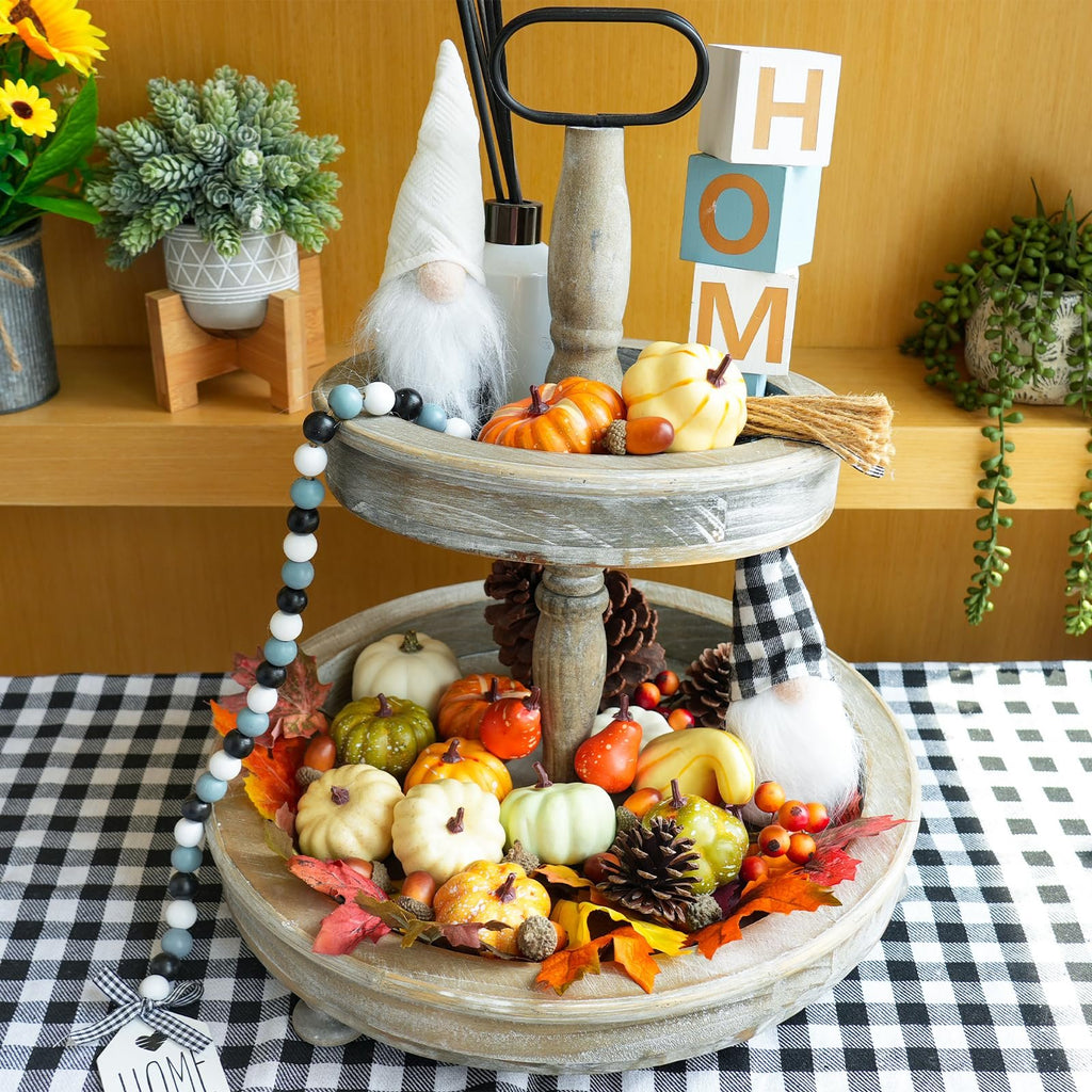 Tiered tray fall decor with artificial pumpkins, gourds, pinecones, acorns, and maple leaves, topped with gnomes and 'HOM' blocks.