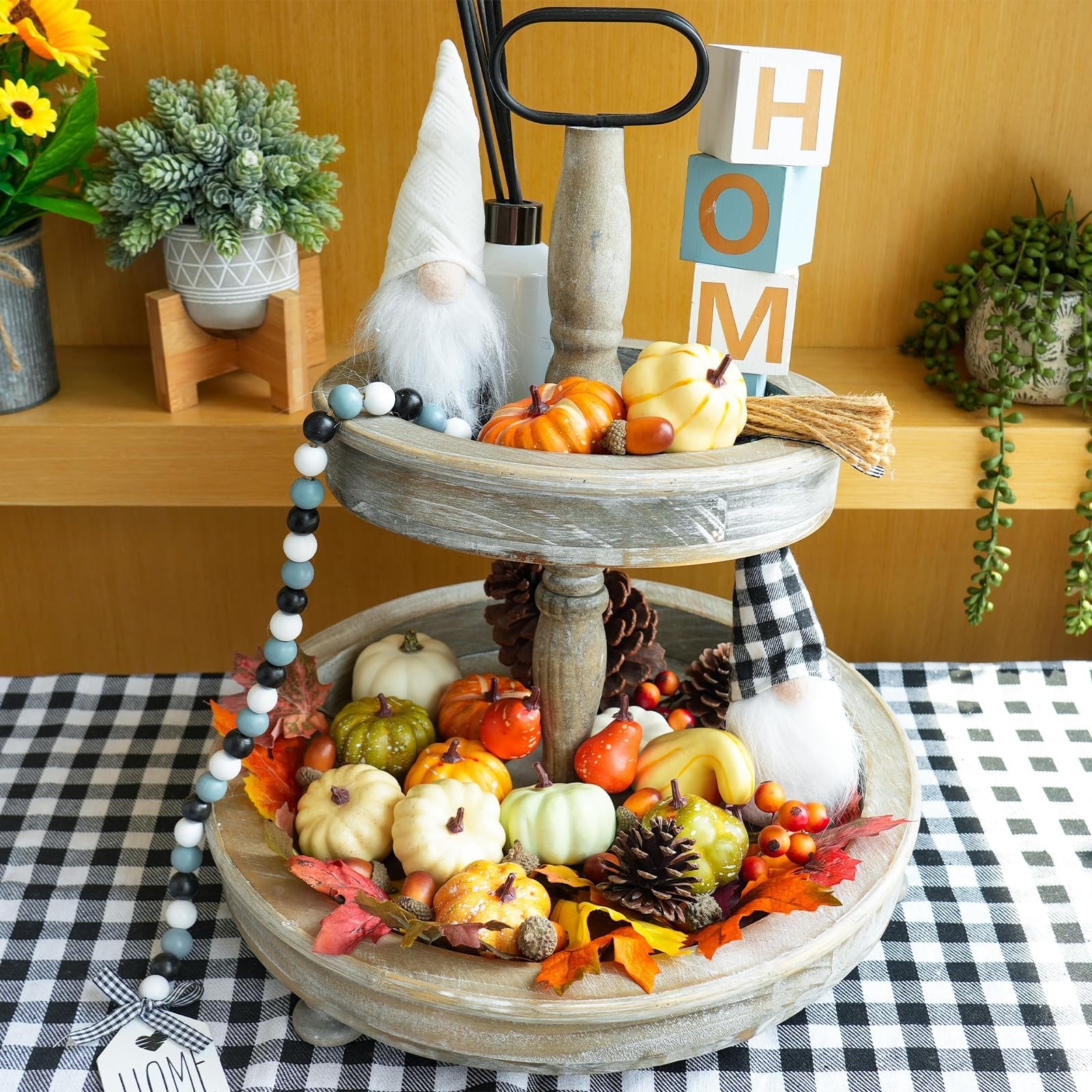 Tiered tray fall decor with artificial pumpkins, gourds, pinecones, acorns, and maple leaves, topped with gnomes and 'HOM' blocks.